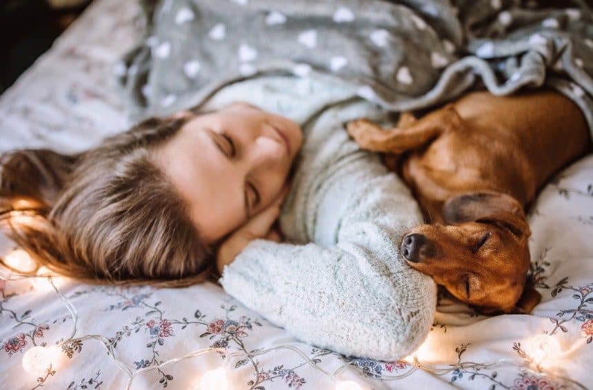 A young woman sleeping with her puppy in bed