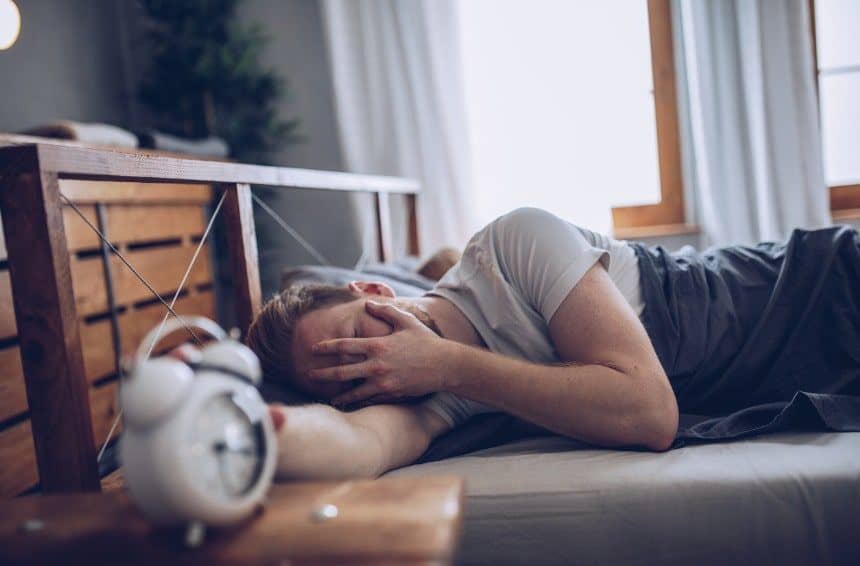 A young man disturbed by morning alarm clock set to fix sleep schedule