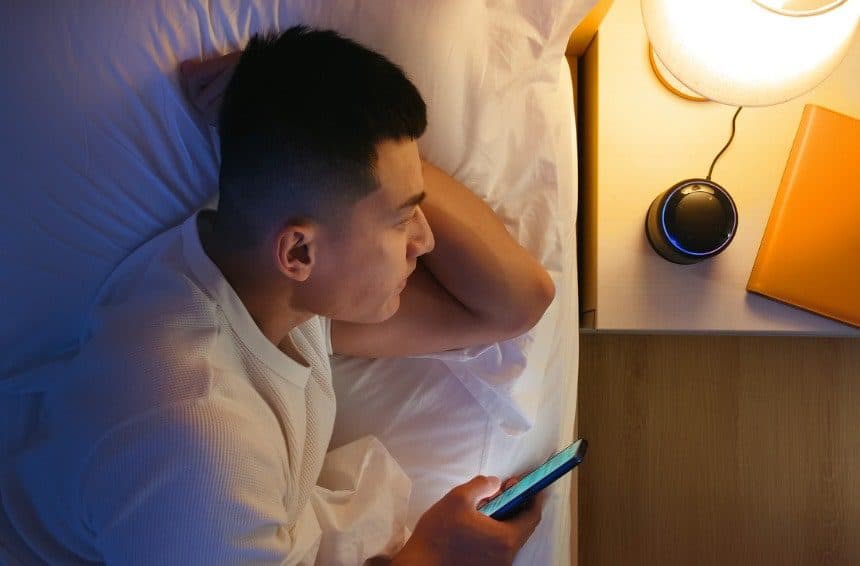 A young man staring at the light of the lamp beside his bed